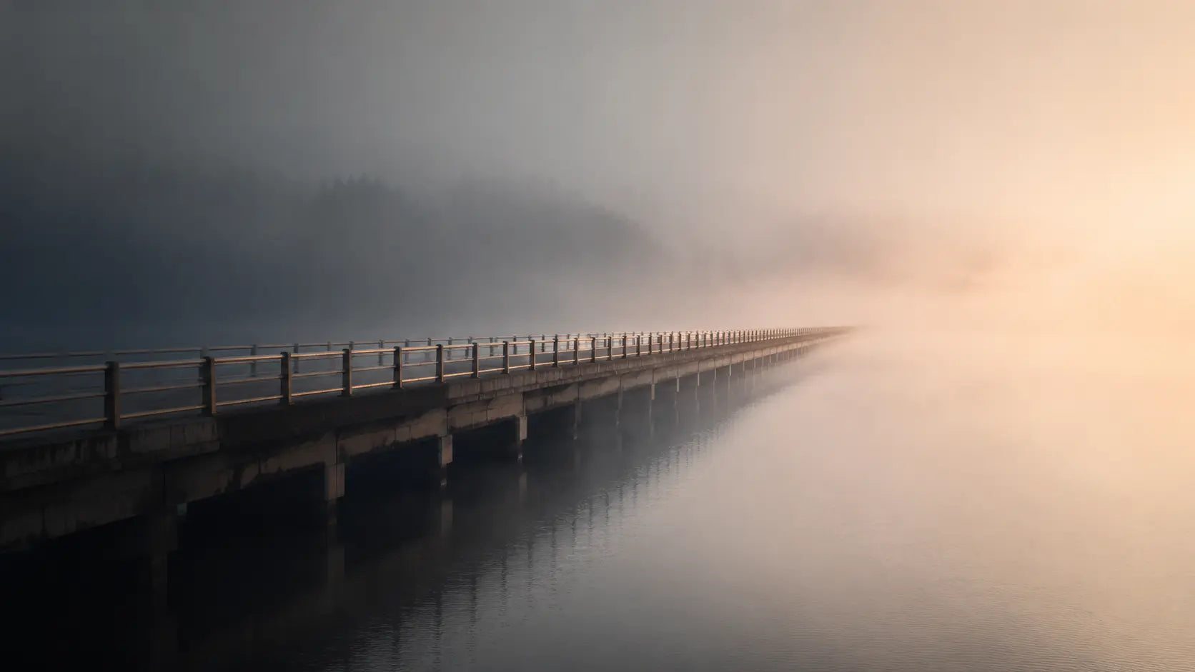 A bridge disappearing into mist over calm water